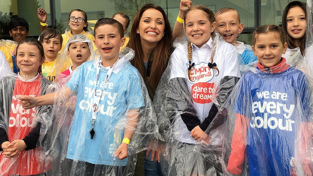 Presenter Natalie smiles as she poses for a photo with members of the choir, who are wearing waterproof ponchos because of the rain