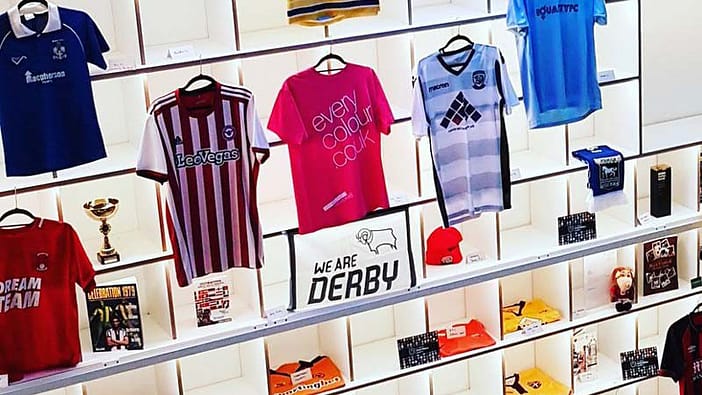 Close up showing magenta Everycolour T-shirt on display with other football shirts and memorabilia